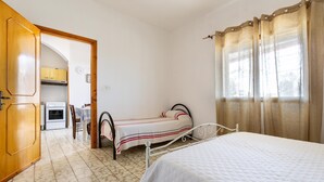 A bedroom with a bed, a small table, and a chair. There is a kitchen area visible through an open door. - 3309 Villetta Mare Fuori - Appartamento Piccolo by Barbarhouse (Porto Cesareo)
