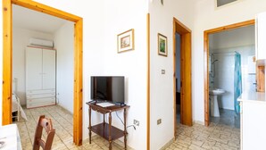 A room with a television on a wooden stand, a white wardrobe, and a bathroom with a sink and shower. - 3309 Villetta Mare Fuori - Appartamento Piccolo by Barbarhouse (Porto Cesareo)