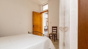 A bedroom with a bed, a wooden door, a chair, and a view of a dining area. - 3310 Villetta Mare Fuori - Appartamento Grande by Barbarhouse (Porto Cesareo)