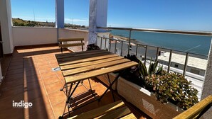 A balcony with a wooden table and chairs, a potted plant, and a view of the sea. - STE003 Riverview 4 Bedroom House, with Private Pool (Ayamonte)
