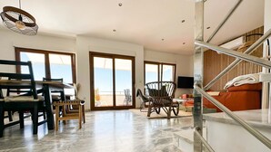 A spacious living area with a dining table, chairs, and a sofa. There is a balcony with a view, and a staircase with a railing. - STE003 Riverview 4 Bedroom House, with Private Pool (Ayamonte)