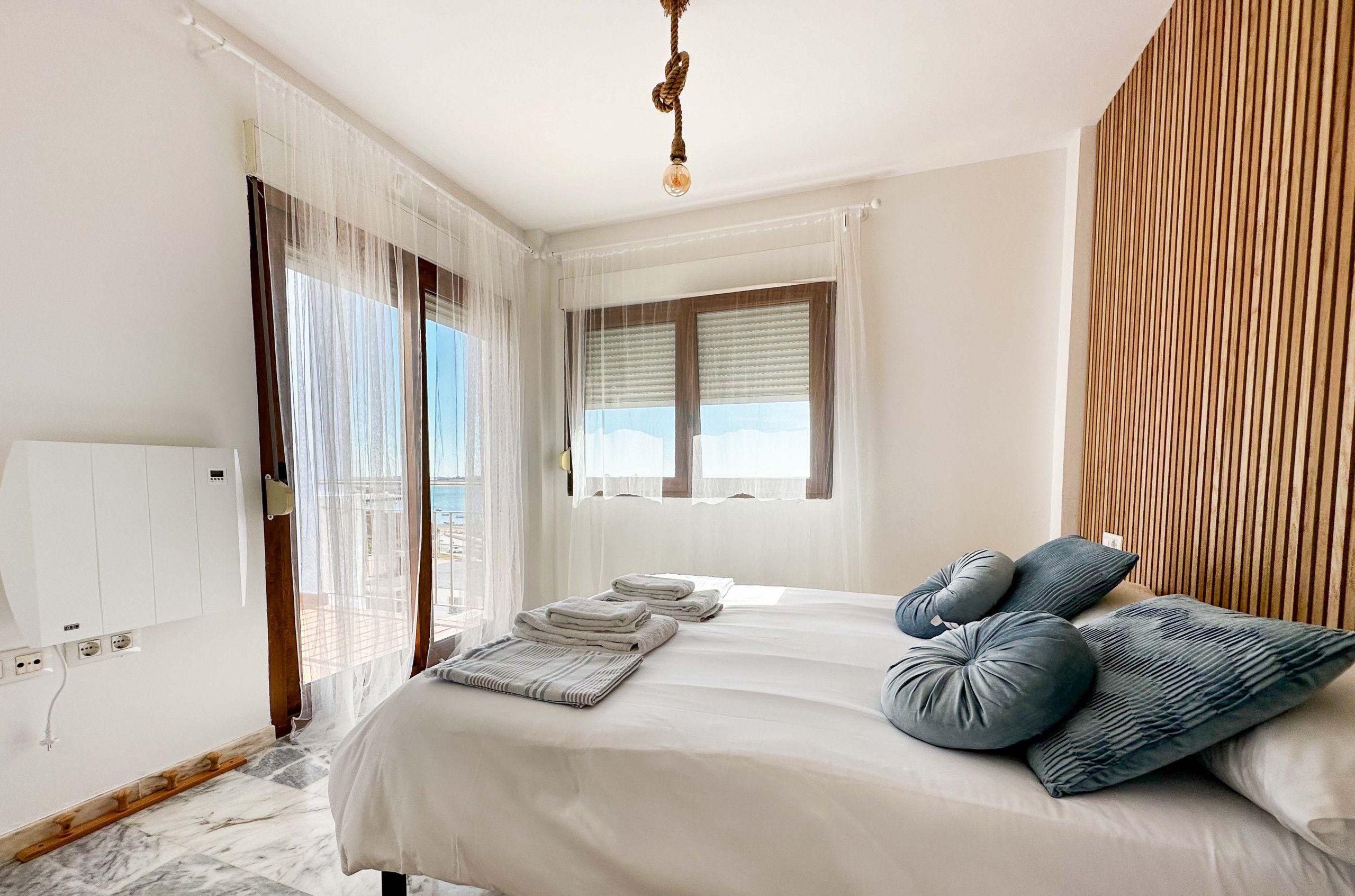 Une chambre à coucher avec un lit, une fenêtre avec des stores, un mur recouvert de panneaux de bois et un luminaire au plafond.