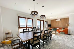 Un comedor amplio con una mesa y sillas de madera, un ventanal con vistas, y una zona de estar moderna con un sofá y una lámpara de pie.