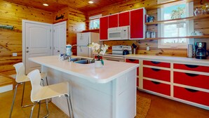 Una cucina compatta con pareti in legno, mobili bianchi e rossi, un'isola centrale con posti a sedere e una finestra con vista.