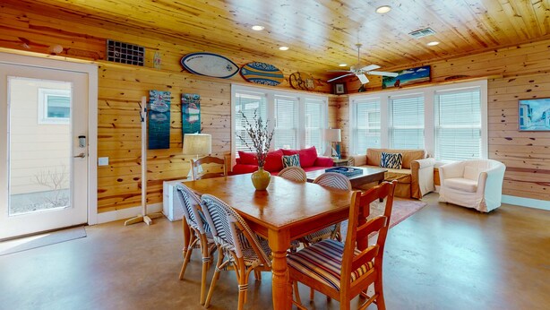 Un'ampia stanza con soffitto in legno, un tavolo da pranzo con sedie, un divano e una poltrona bianca.