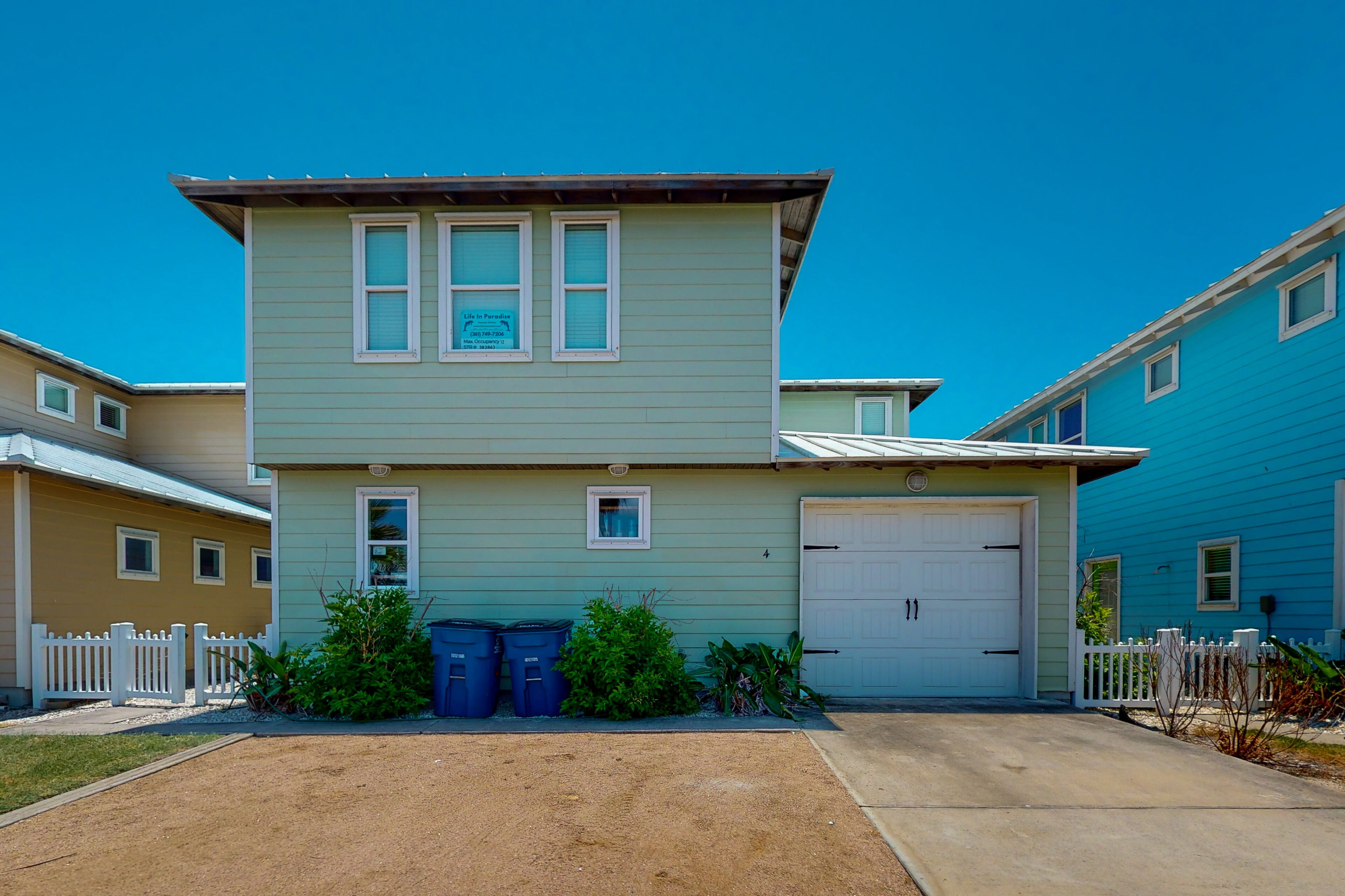A two-story building with a garage, a small porch, and a fenced yard.