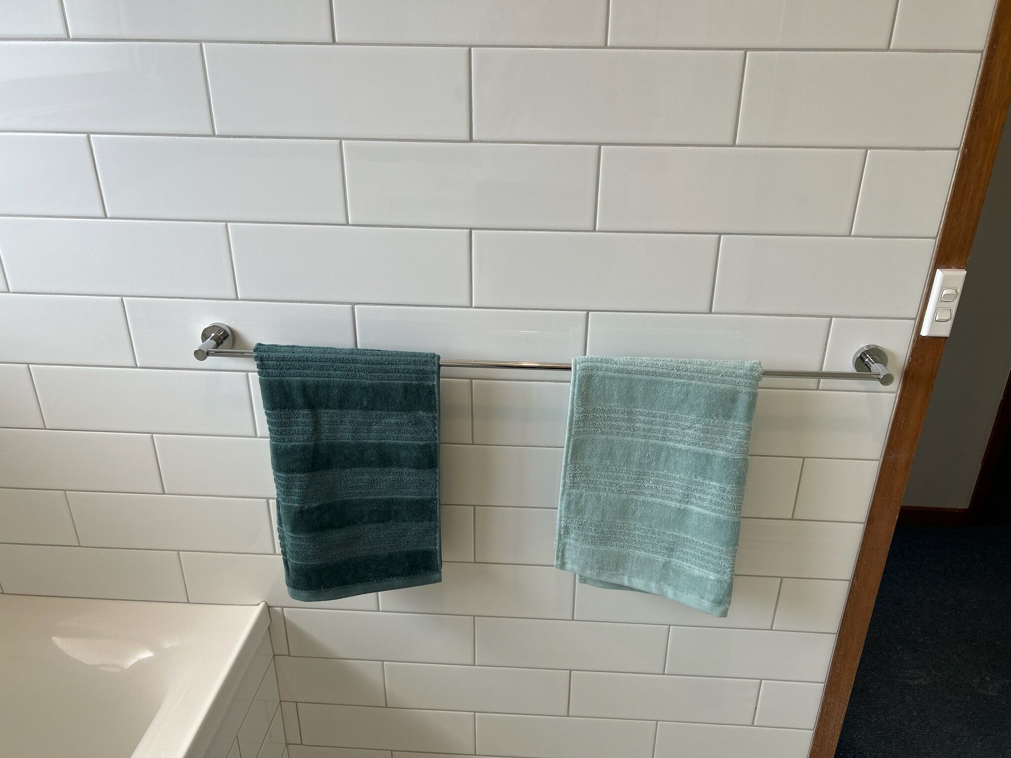 Un bagno con pareti rivestite di piastrelle bianche e due asciugamani appesi a un portaserviti in metallo.