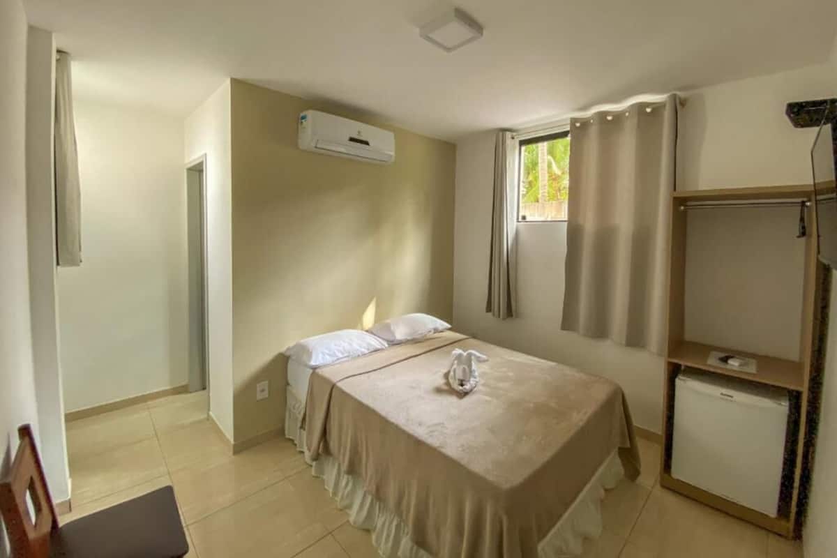 A bedroom with a bed, a small desk, a wardrobe, and an air conditioning unit.
