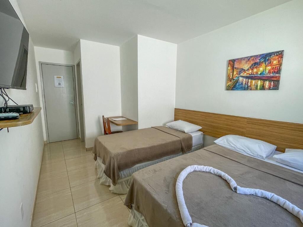 Una habitación de hotel con dos camas, un cuadro en la pared, un escritorio y una puerta que da a otra habitación.