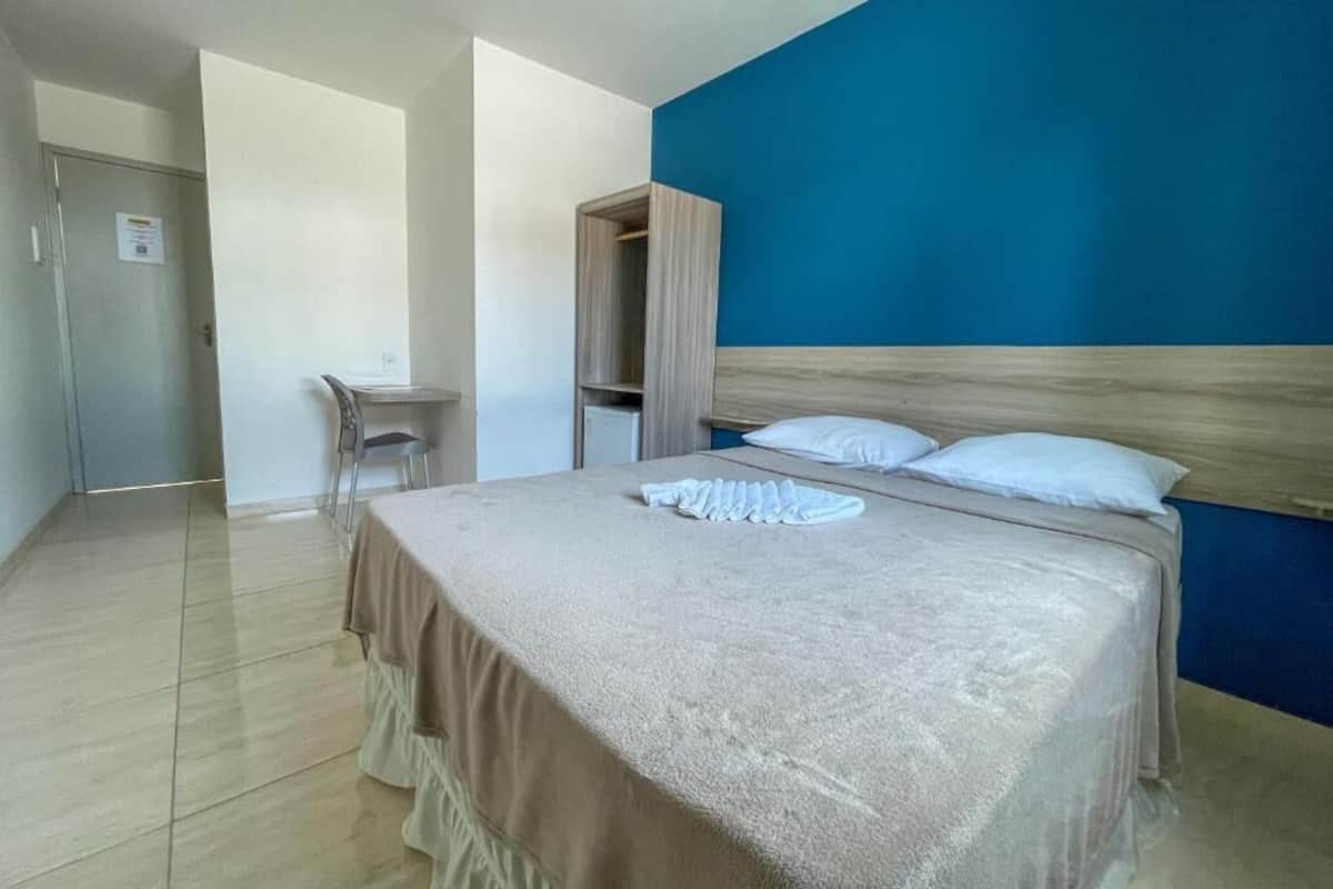 A bedroom with a bed, a chair, a small table, and a wardrobe.
