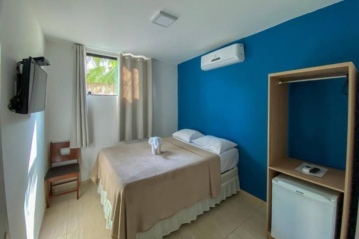 A room with a bed, a desk, a chair, a TV, and an air conditioning unit.