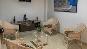 Una sala de estar con muebles de mimbre, un televisor de pantalla plana, una cafetera y un cuadro de una escena costera.