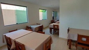 Un comedor con varias mesas y sillas, ventanas amplias que dejan entrar luz natural y suelo de baldosas.