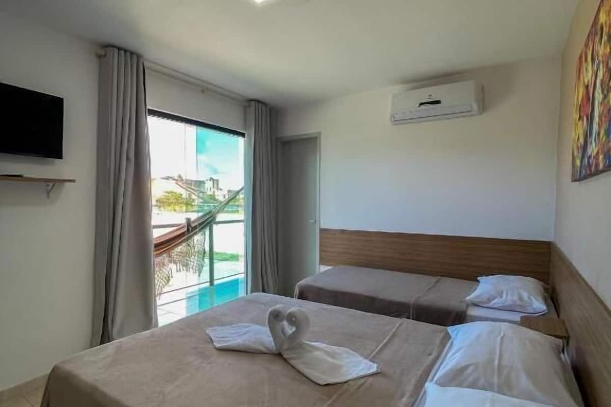 A hotel room with two beds, a TV, an air conditioning unit, and a painting on the wall.