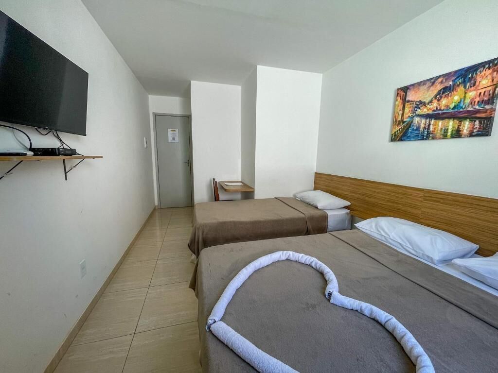 Quarto de hotel com duas camas, uma televisão fixada na parede, um quadro e uma porta que dá para outro quarto.