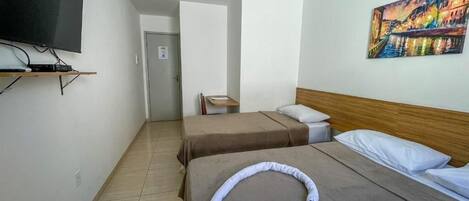 Quarto de hotel com duas camas, uma televisão fixada na parede, um quadro e uma porta que dá para outro quarto.