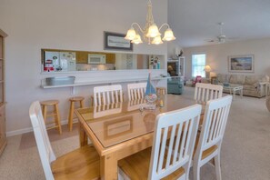 A dining area with a glass-top table, white chairs, and a chandelier. - Stay at Reel Estate, a spacious 3-bedroom home in Oak Island, perfect for beach lovers! (Oak Island)