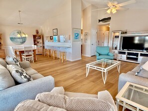 Amplia sala de estar con televisor grande, asientos cómodos y un comedor con sillas y taburetes de madera.