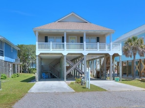 A two-story house with a balcony, a covered entryway, and a staircase leading to the upper floor. - Stay at Reel Estate, a spacious 3-bedroom home in Oak Island, perfect for beach lovers! (Oak Island)