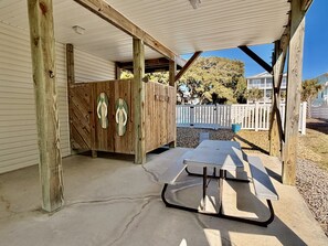 A covered outdoor area with a concrete floor, wooden posts, a picnic table, and a wooden cabinet with flip-flops hanging on it. - Stay at Reel Estate, a spacious 3-bedroom home in Oak Island, perfect for beach lovers! (Oak Island)