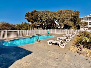 A swimming pool with lounge chairs and a white fence.