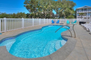 A swimming pool with a white fence, blue chairs, and a building in the background. - Stay at Reel Estate, a spacious 3-bedroom home in Oak Island, perfect for beach lovers! (Oak Island)