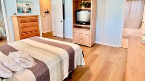 A bedroom with a bed, a dresser, a television on a stand, and a ceiling fan.