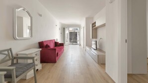 A modern, well-lit hallway with a wooden floor, a red sofa, a white dresser, and a TV on a wooden cabinet. - 3306 Villino Terracielo su Barbarhouse (Porto Cesareo)
