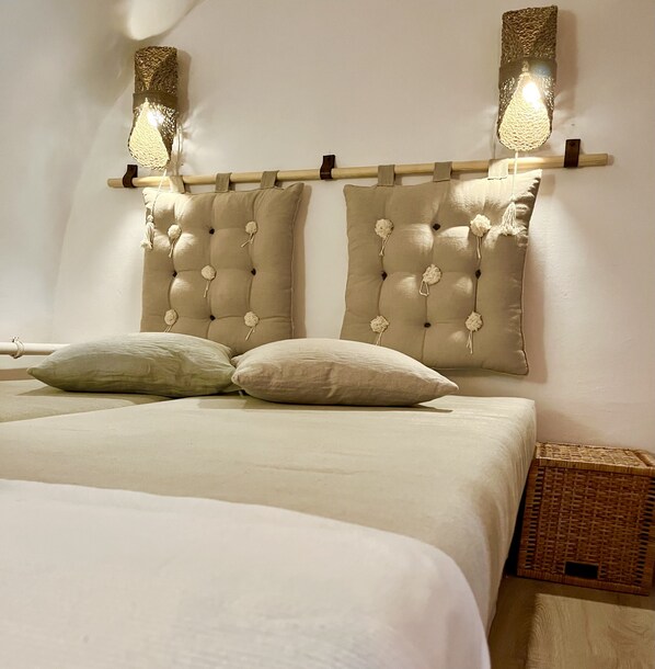 A bed with a tufted headboard, two wall-mounted lamps, and a wicker basket.