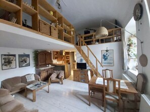 A spacious living area with a high ceiling, wooden furniture, a staircase, and a kitchen area.