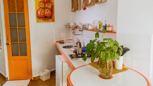 Une cuisine avec des armoires blanches, un évier et une cuisinière. On y trouve une plante sur le comptoir et une porte avec une fenêtre.