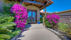 Uma casa com varanda coberta, porta com painéis de vidro e trepadeiras de bougainvillea rosa vibrantes.