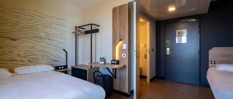 Una habitación de hotel moderna con dos camas, un escritorio, un armario y la puerta del baño.