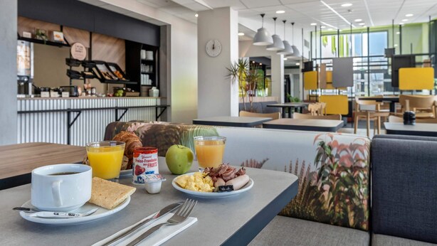 A breakfast setting with a table set for two, including croissants, scrambled eggs, bacon, and juice.