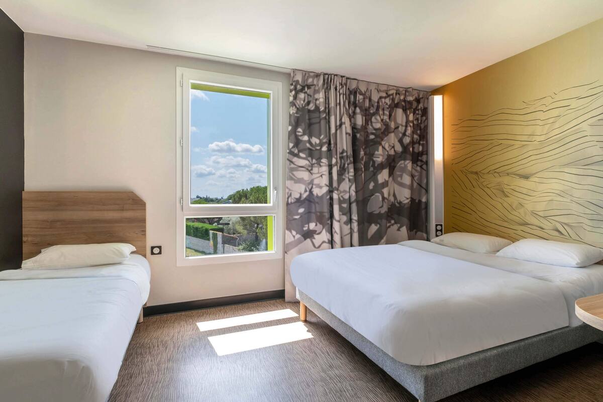 A hotel room with two beds, a large window with a view, and a modern wall design.