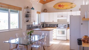 A modern kitchen with white cabinets, a glass dining table, and a wooden ceiling. - Stormfront Guesthouse-Downtown, Hot Tub, Arcade Games (Tofino)