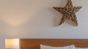 A neatly made bed with white linens, a wooden headboard, a star-shaped wall decoration, and a bedside table with a lamp. - Stormfront Guesthouse-Downtown, Hot Tub, Arcade Games (Tofino)
