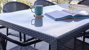 A table with a book and a mug, surrounded by wicker chairs, set on a balcony with a mountain view. - Stormfront Guesthouse-Downtown, Hot Tub, Arcade Games (Tofino)