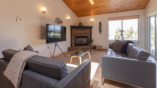 A modern living room with a fireplace, leather sofas, a TV, and a large window with a telescope. - Stormfront Guesthouse-Downtown, Hot Tub, Arcade Games (Tofino)