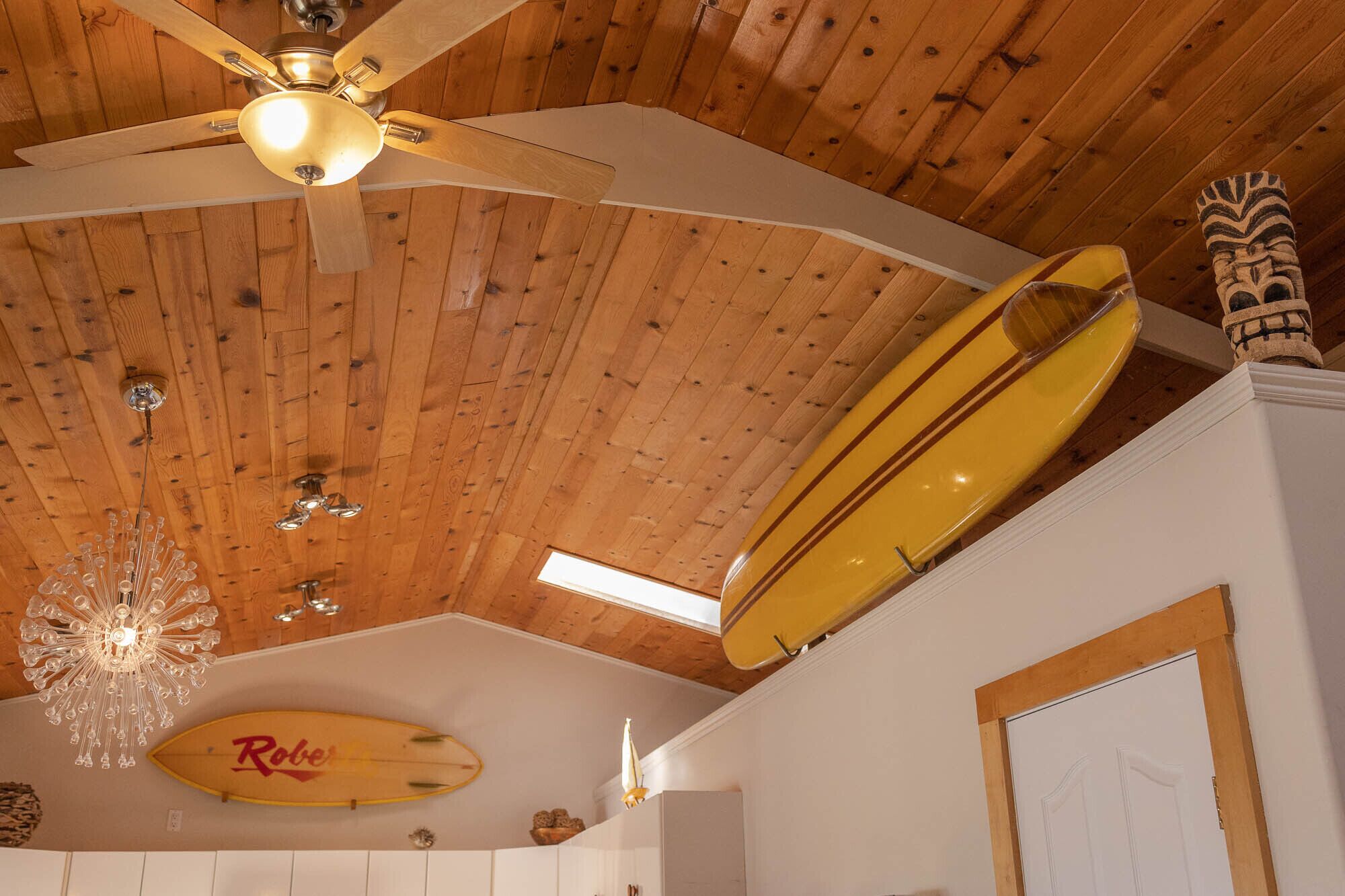 Ein Zimmer mit Holzboden, Deckenventilator, Surfbrett und einer Kronleuchter.