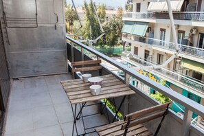 Ein Balkon mit Tisch und Stühlen, Blick auf benachbarte Gebäude und eine an der Wand stehende Leiter.