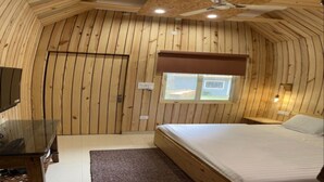 Een kamer met houten lambrisering, een bed, een plafondventilator, een raam en een televisie.