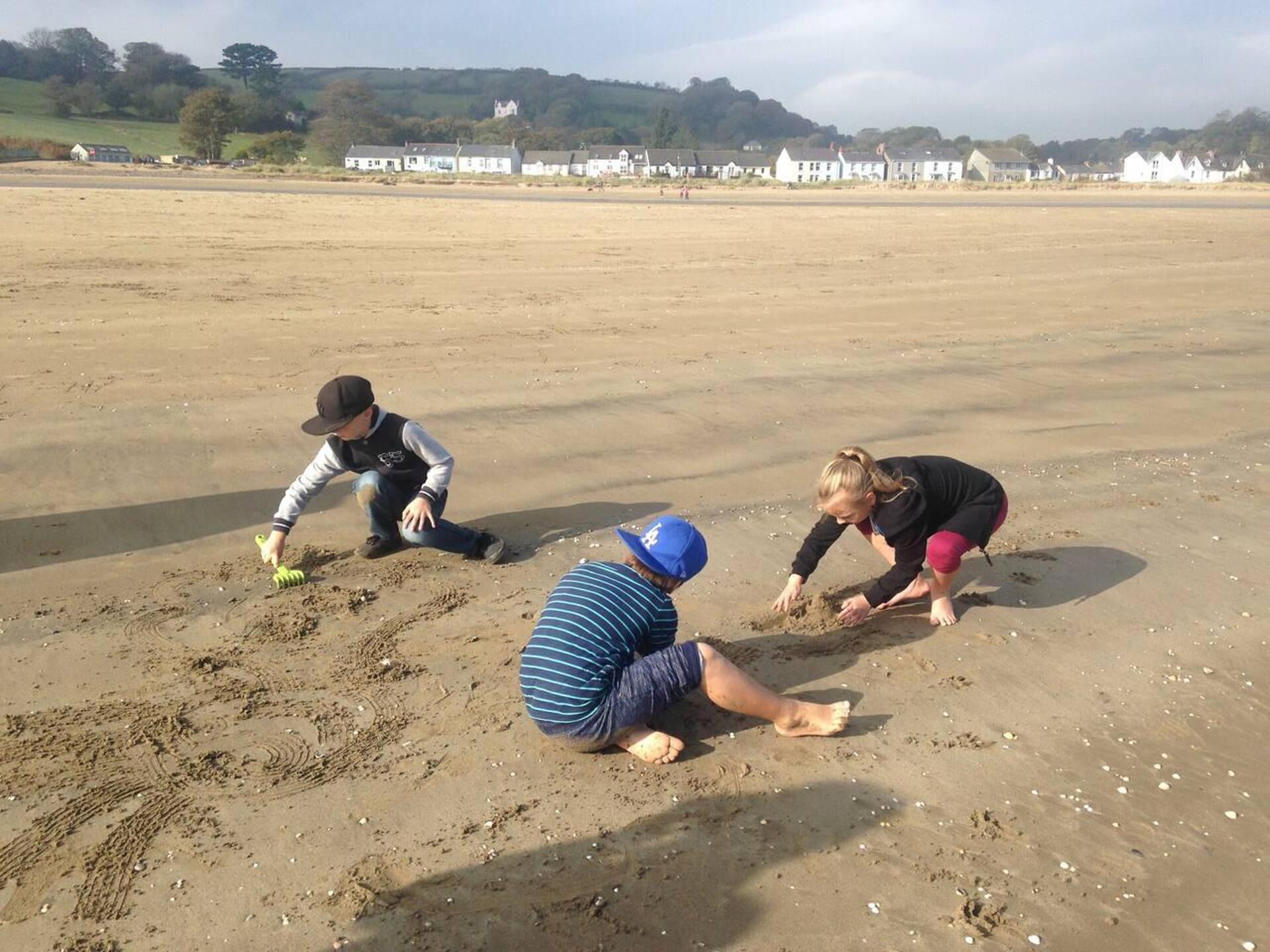 Three people playing on a sandy beach with houses in the background.