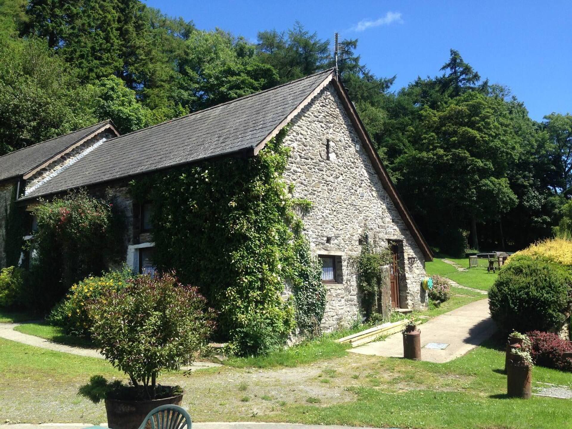 A stone building with a sloped roof, surrounded by greenery and a clear path leading to it.