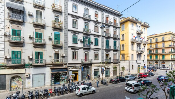Un edificio de varios pisos con balcones, una tienda en la planta baja y vehículos estacionados.