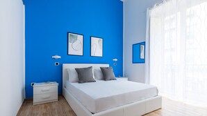 Un dormitorio con cama blanca, paredes azules y suelo de madera.