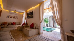 A spacious living room with a sofa set, a dining table, and a view of an outdoor pool area. - Riad Dar Bayane (Marrakech)
