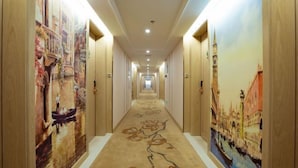 A hotel hallway with a carpet featuring a floral design and walls adorned with paintings of European scenes. - Vienna International Hotel (Gaoxin Keji Road Metro Station Store) (Xi'an)