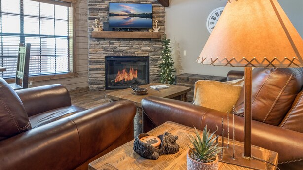 A cozy living room with leather sofas, a fireplace, a television, and a table with decorative items.