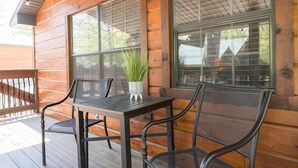 A wooden cabin with a deck, a table with chairs, and a potted plant.